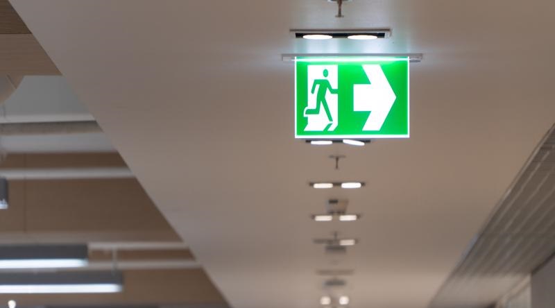 Green fire escape sign hang on the ceiling in the office.